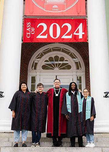 BSU President Fred Clark with four Presidential Scholars, standing on the steps of Boyden Hall in front of a Class of 2024 banner